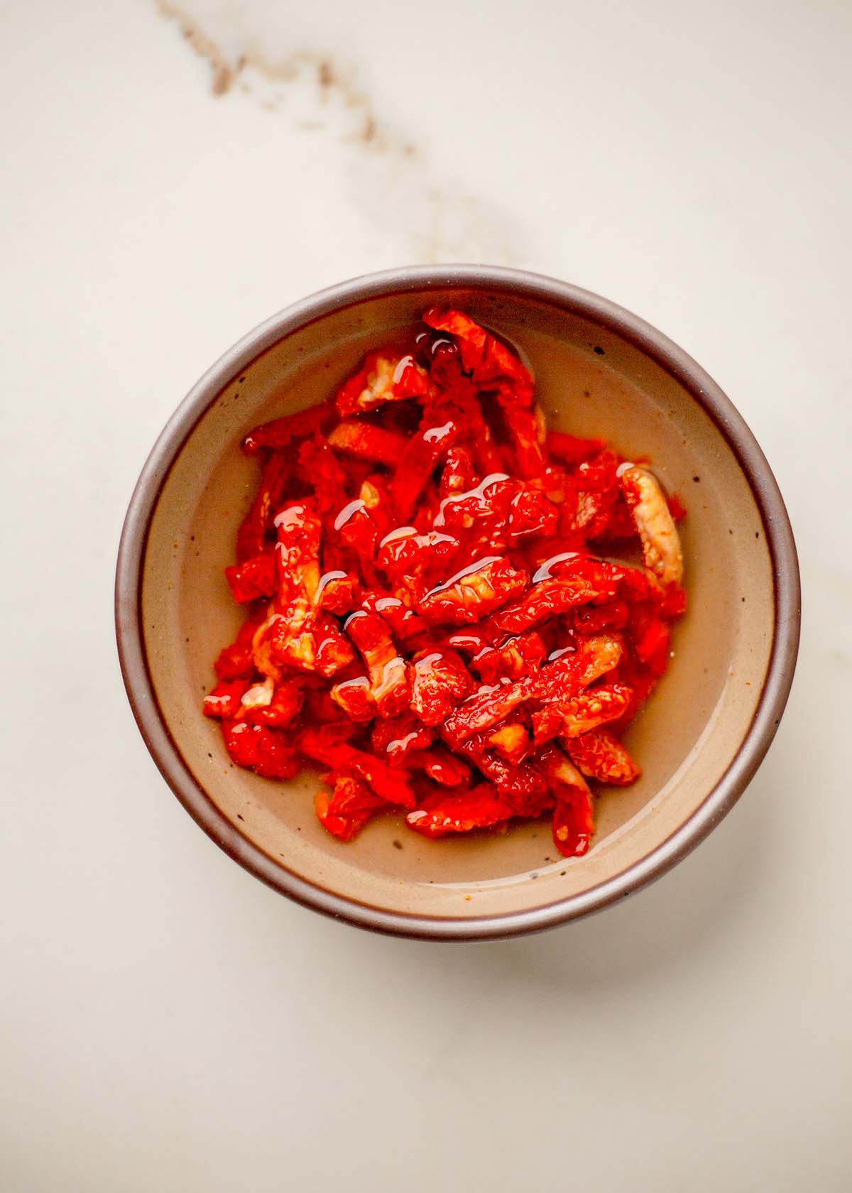 A brown bowl filled with bright red sun-dried tomatoes in water.