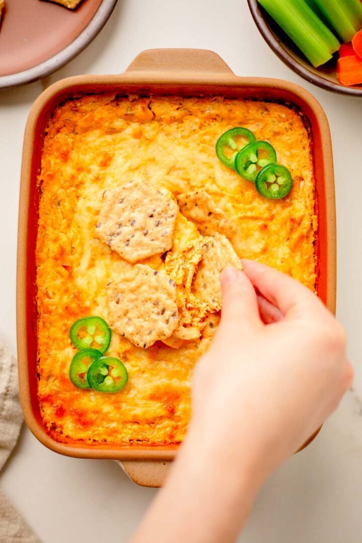 Hand dipping into buffalo chicken dip with gluten-free crackers