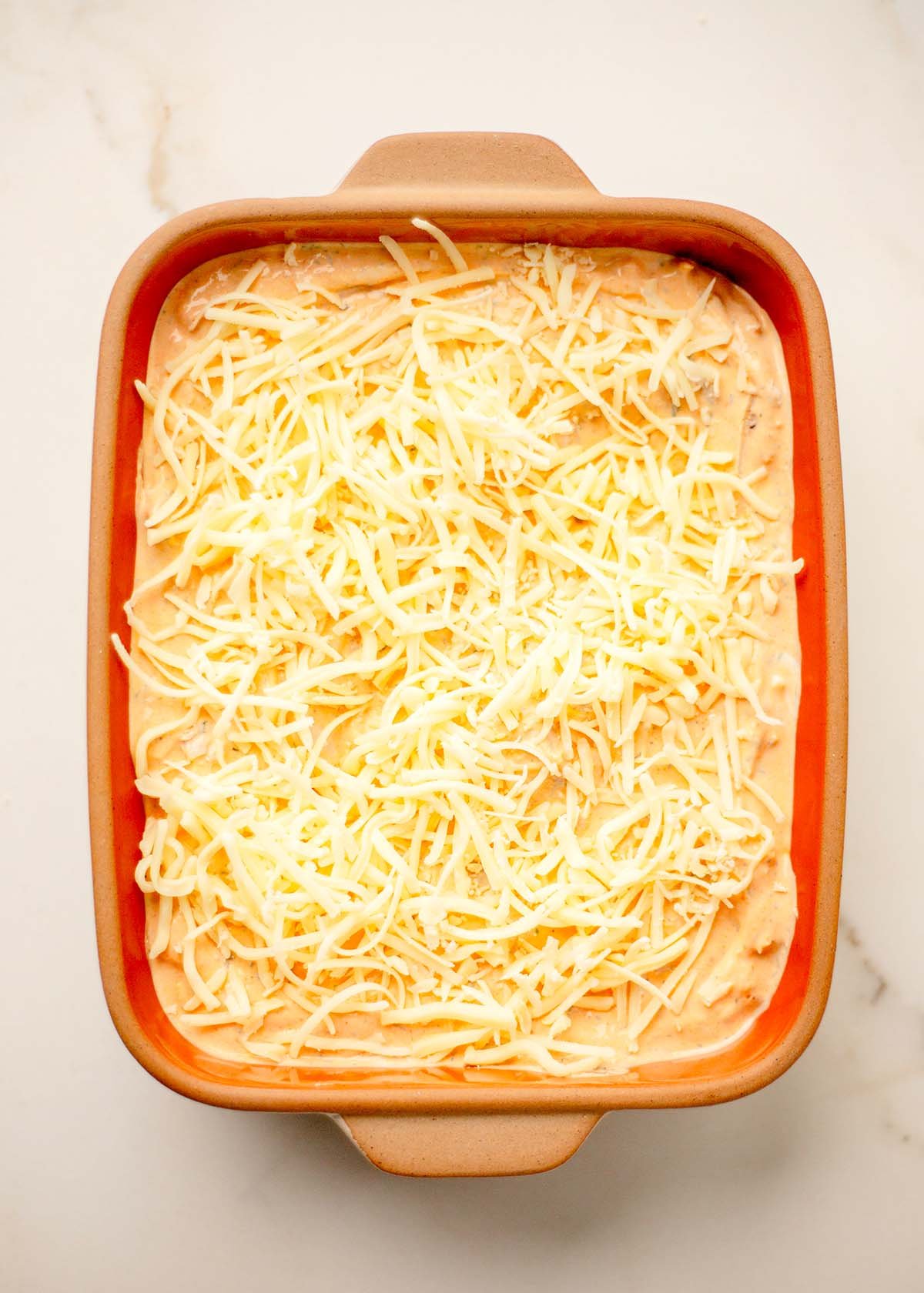 Buffalo chicken dip spread into a baking dish before baking