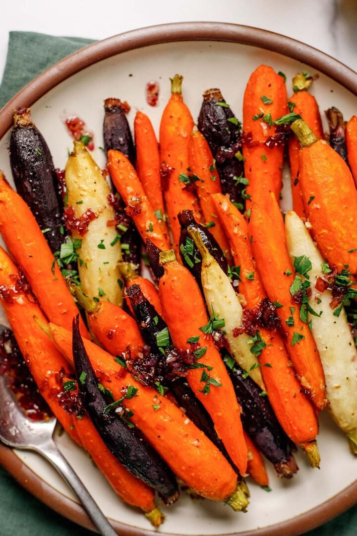 Roasted Rainbow Carrots on a plate garnished with shallot honey jam and fresh parsley