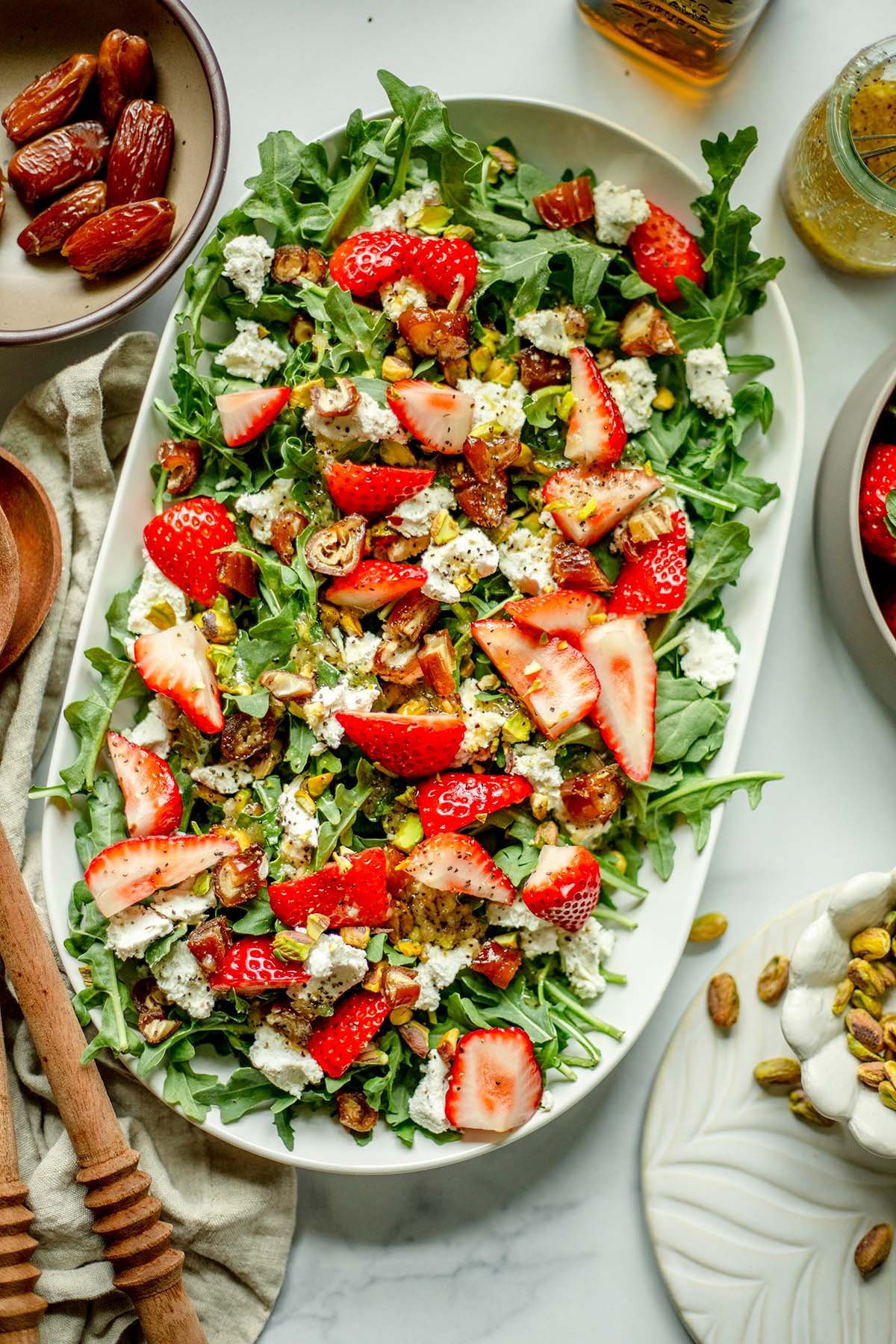 Strawberry Arugula Salad with a bowl of pistachios, strawberries, and wooden spoons