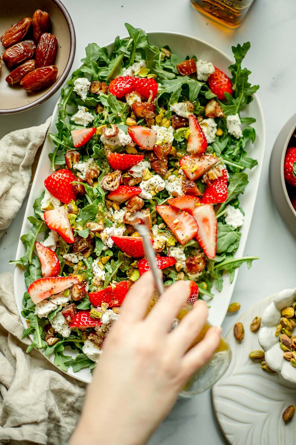 A hand pouring poppy seed vinaigrette over arugula salad