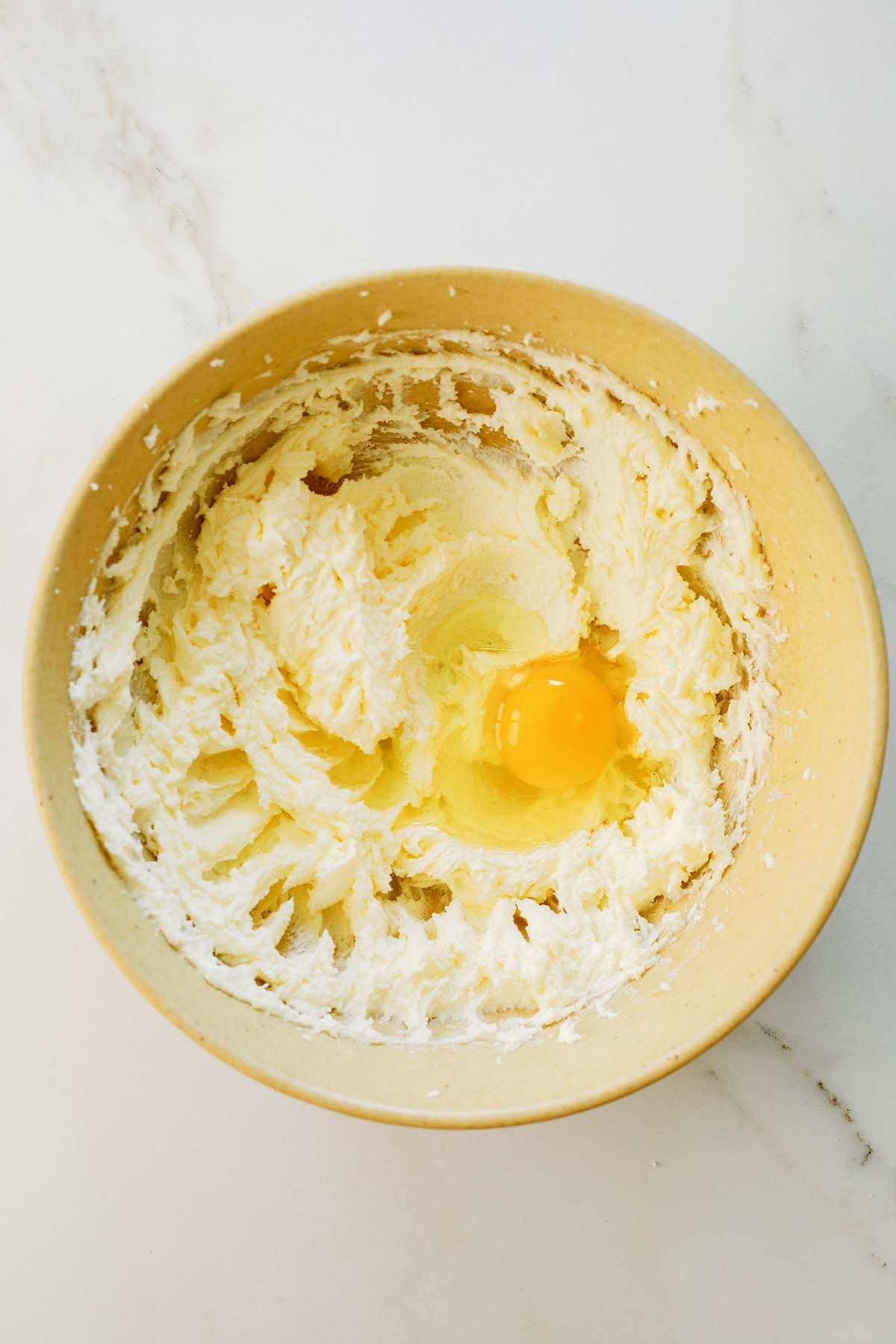 Egg being added to creamed butter and sugar mixture in a large bowl.