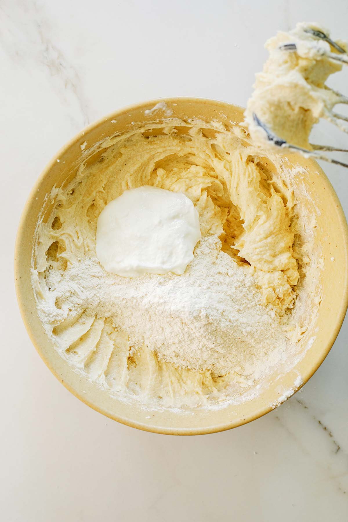 Greek yogurt added to cake batter in a large mixing bowl, alternating with flour