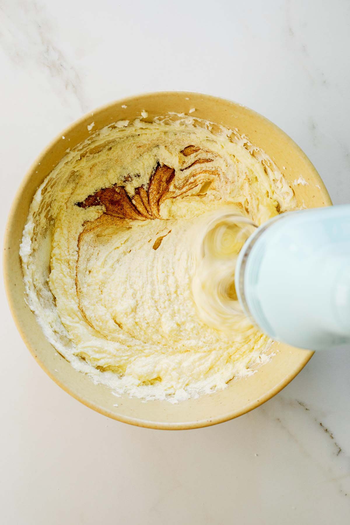 Vanilla extract being poured into cake batter in a large mixing bowl.